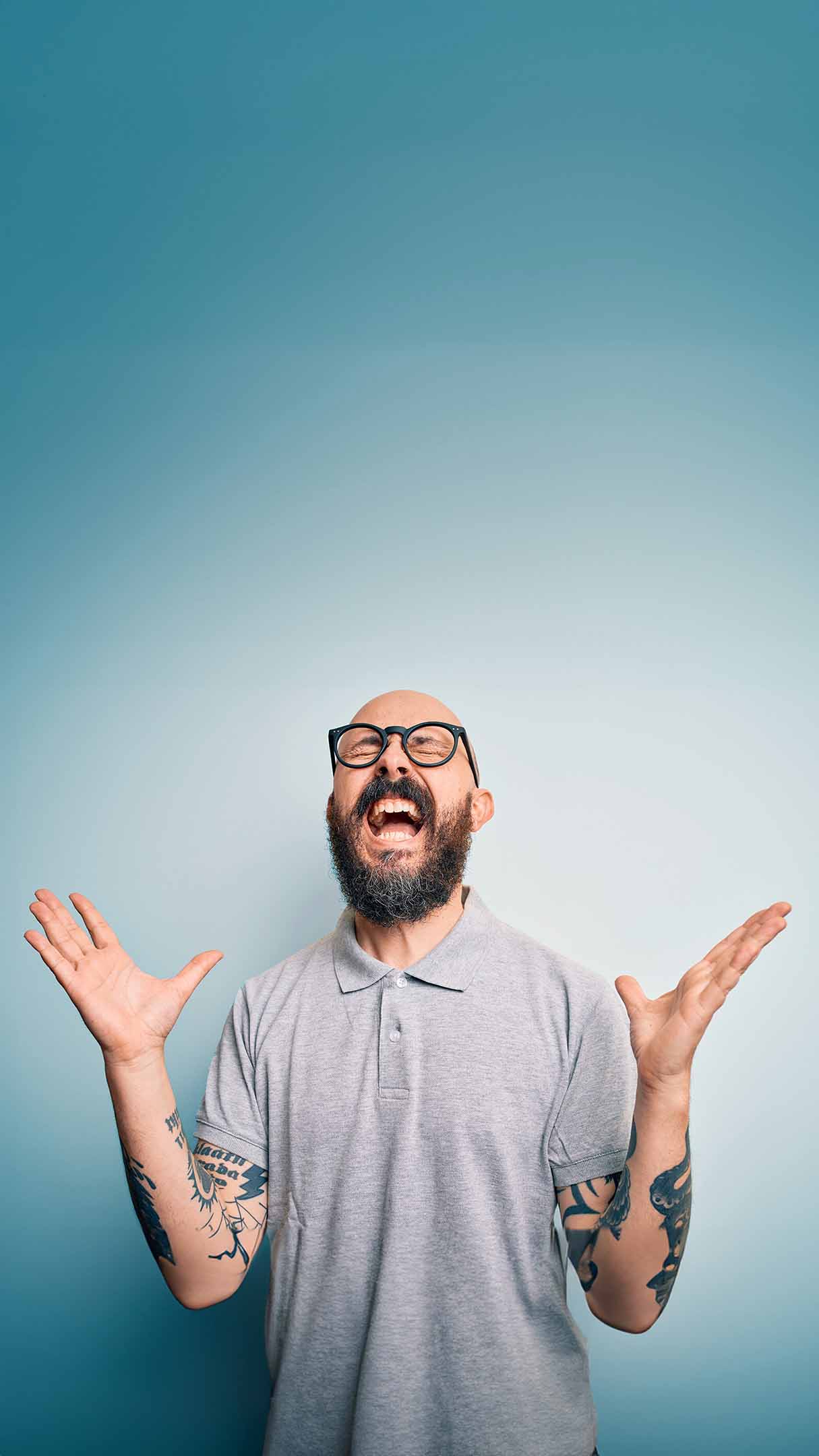 Man with tattoos and glasses raising his hands against a blue background