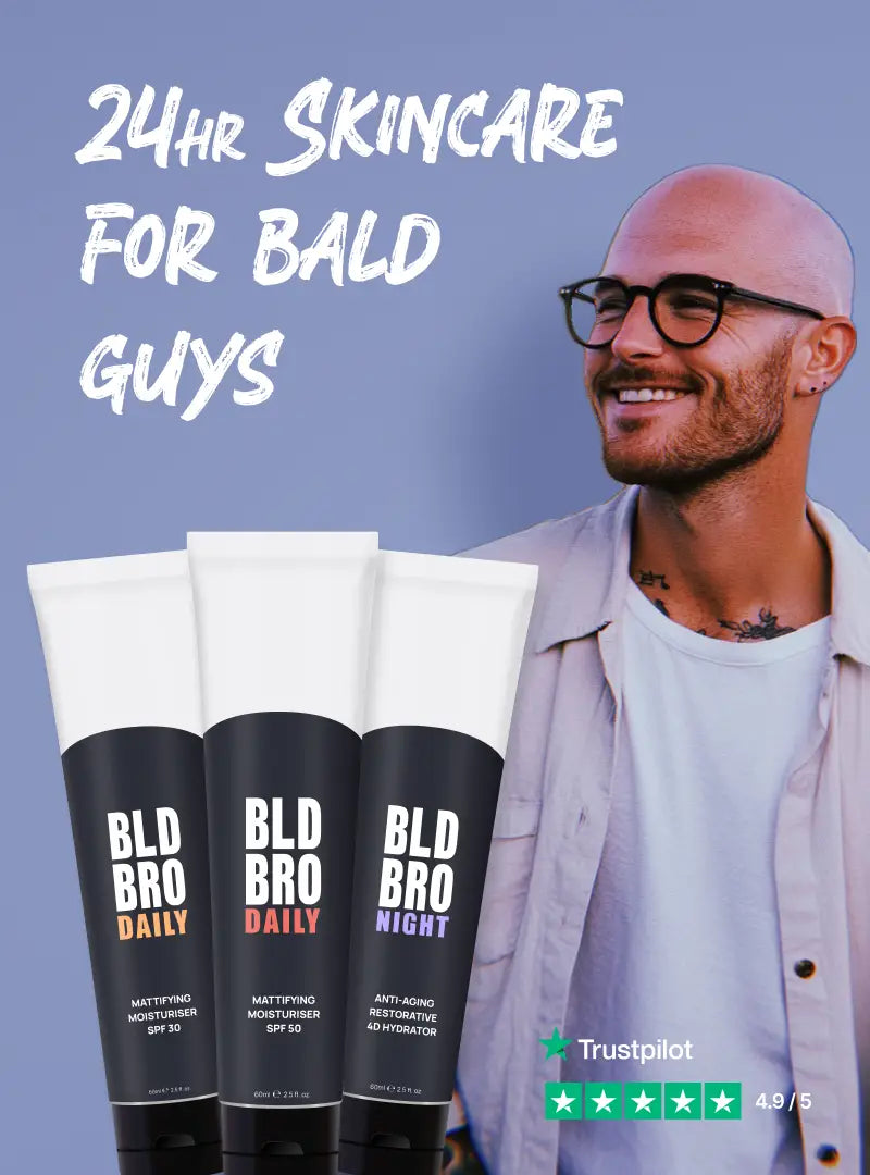 Man with a bald head and glasses standing next to BLD BRO skincare products on a blue background