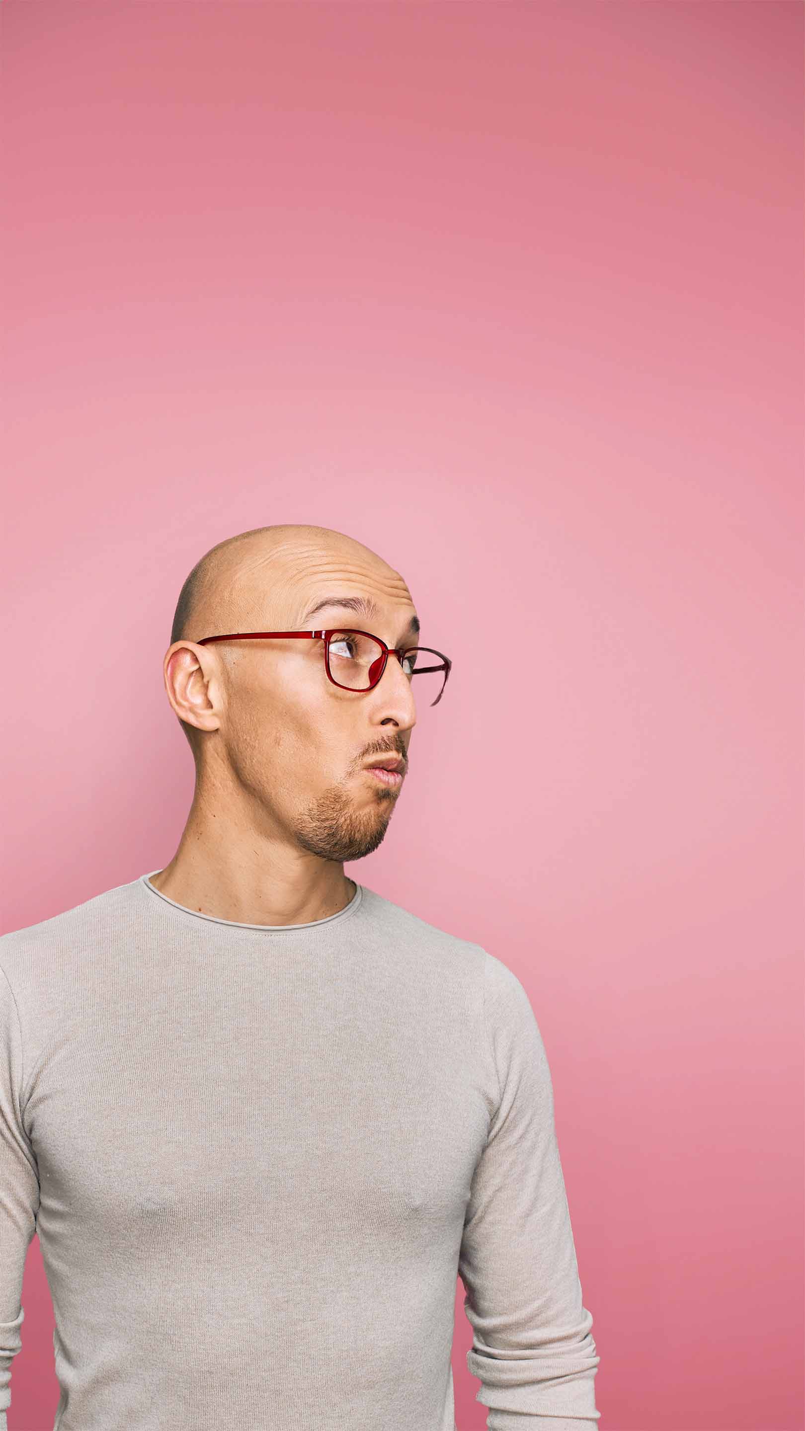 A man with glasses looks up and to the right of screen. He has a bald head and has an interested expression