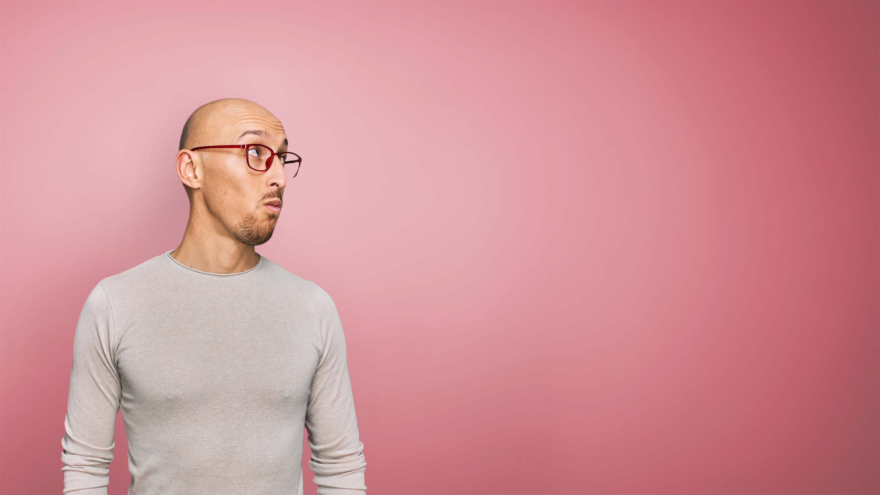 A man with glasses looks up and to the right of screen. He has a bald head and has an interested expression