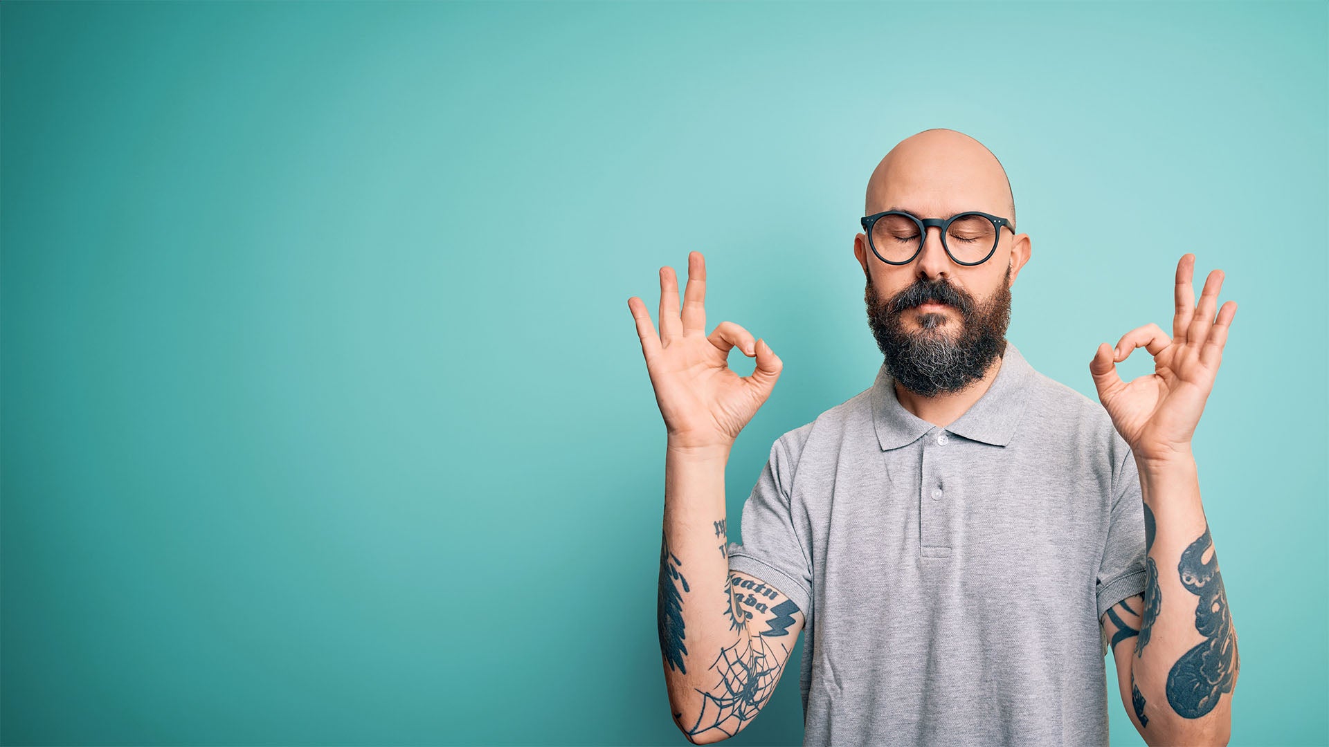 A bald man with glasses does okay peace sign with both hands