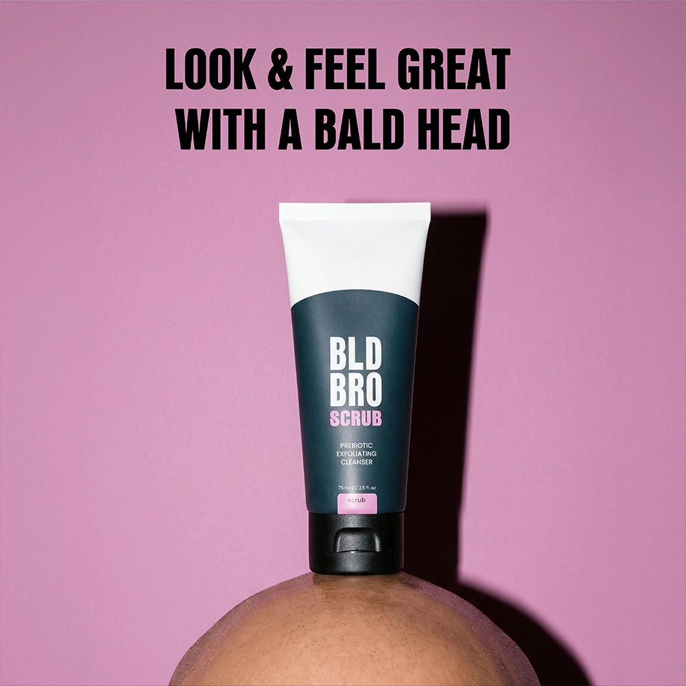 A squeeze tube of BLD BRO SCRUB exfoliating scrub stands upright on a person's bald head against a solid pink background, with bold black text at the top reading 'LOOK & FEEL GREAT WITH A BALD HEAD'.